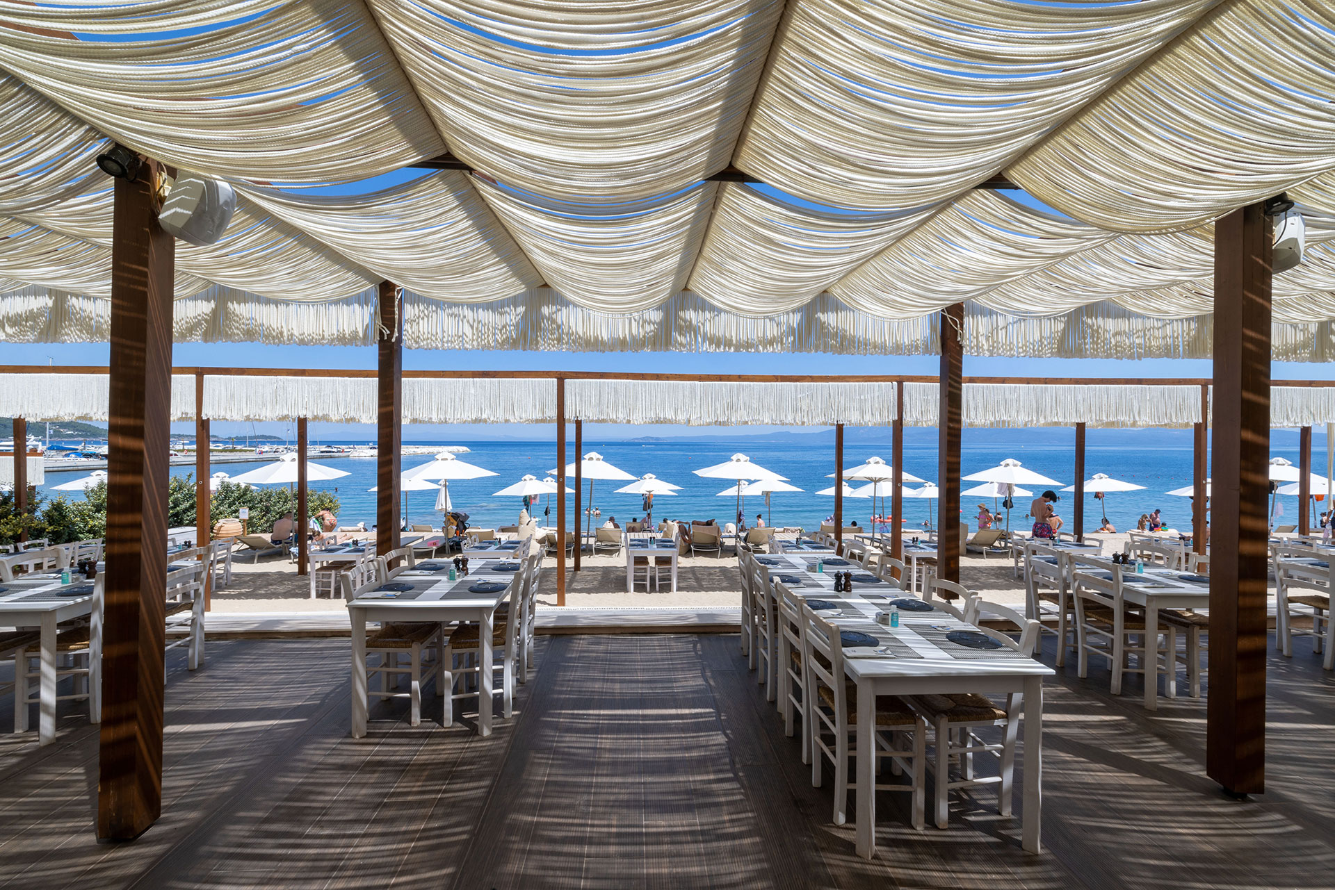 Wide view of Mezedaki beach restaurant seating area with shaded tables and panoramic sea view