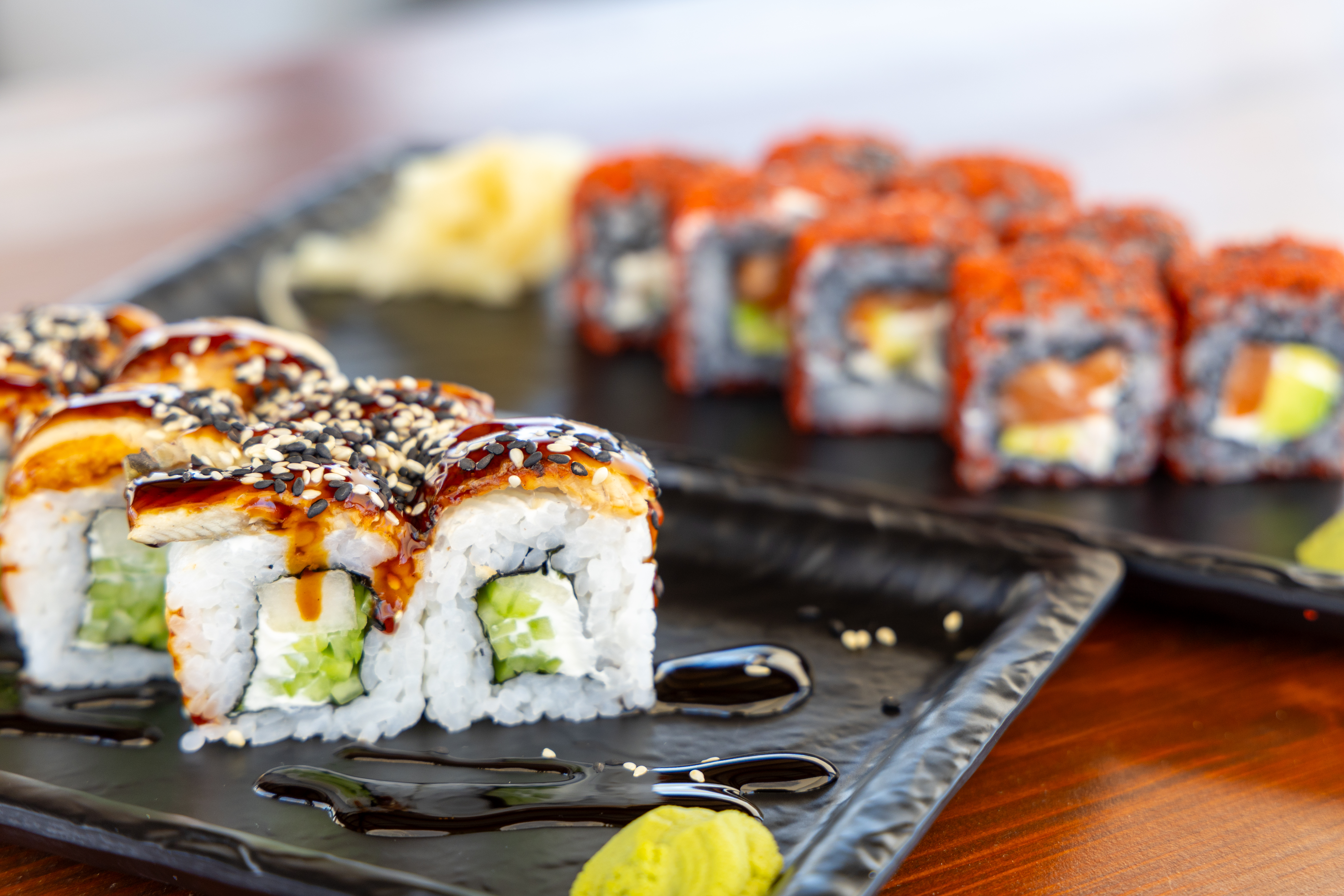 Assorted sushi rolls topped with sesame seeds and soy glaze on black serving plates