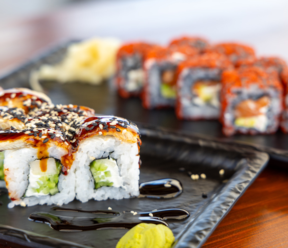 Assorted sushi rolls topped with sesame seeds and soy glaze on black serving plates