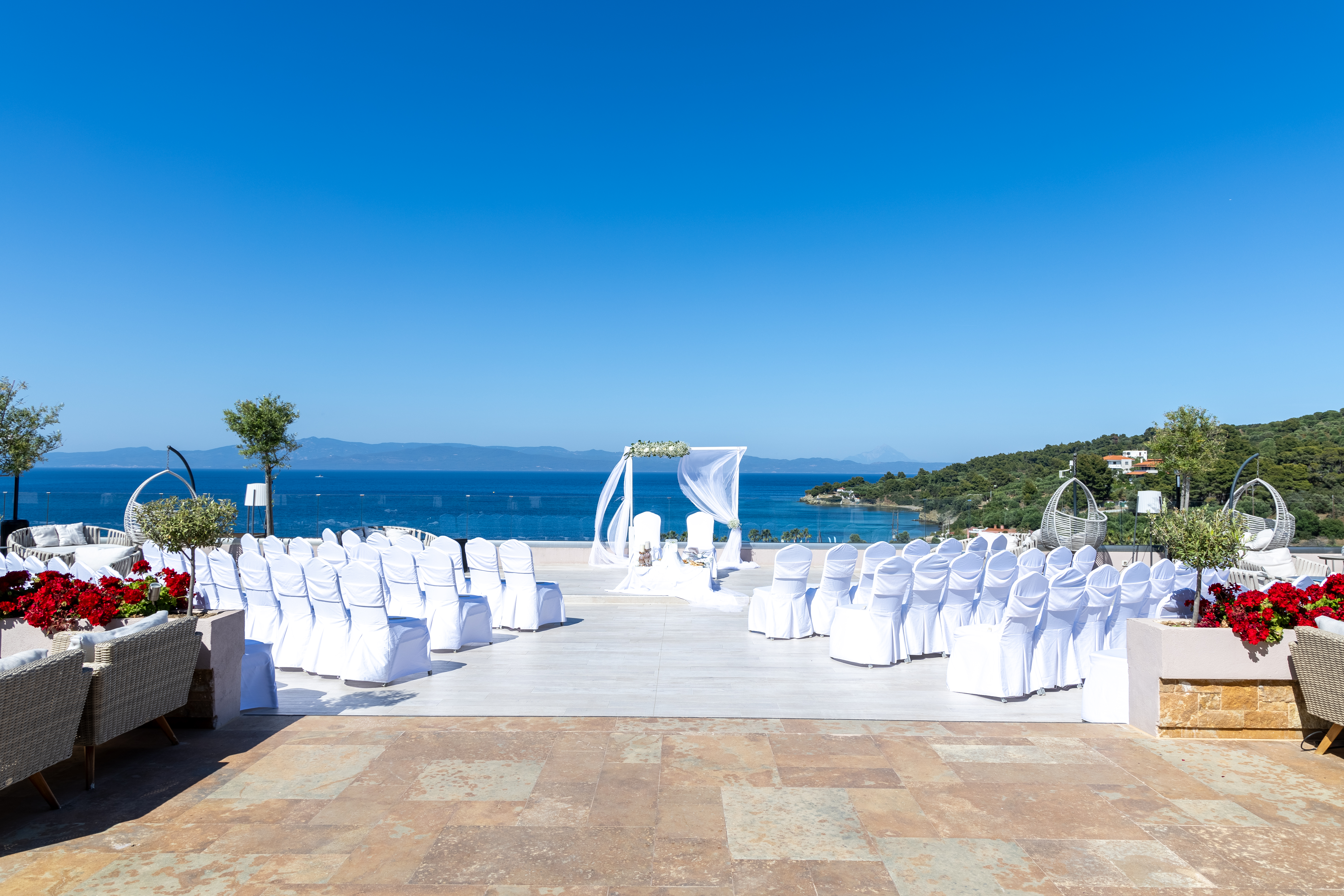 Seaside wedding ceremony setup with white chairs and floral arch overlooking the Aegean