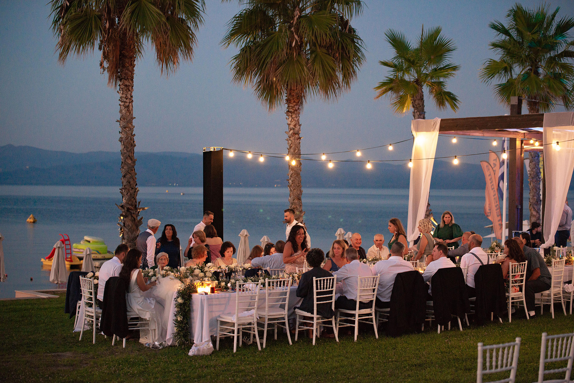 Outdoor seaside wedding dinner under string lights at sunset