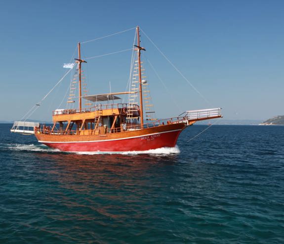 Traditional wooden sailing boat cruising on calm blue water with open deck and island view in the background