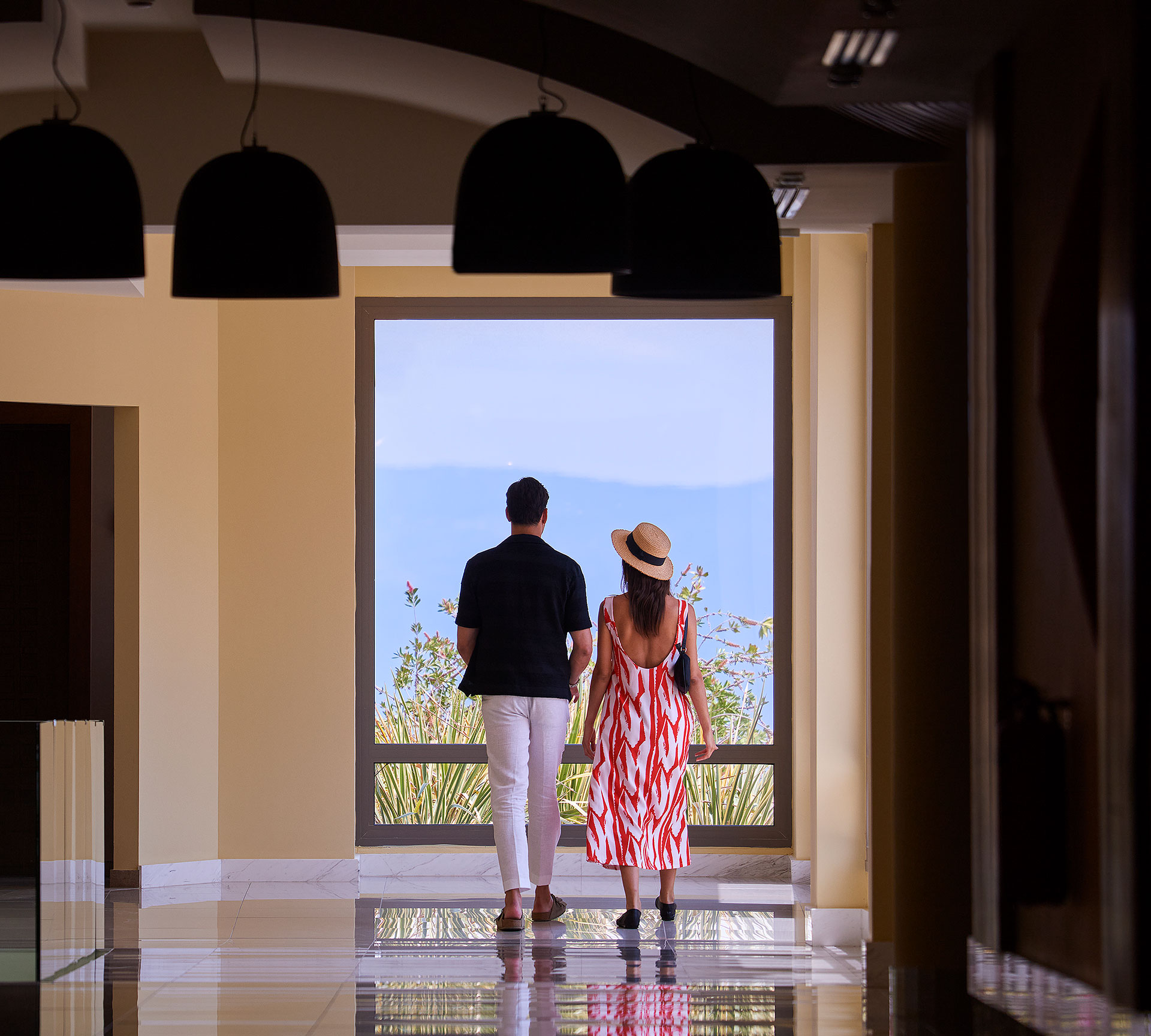 Couple walking hand in hand through elegant hallway with sea view window