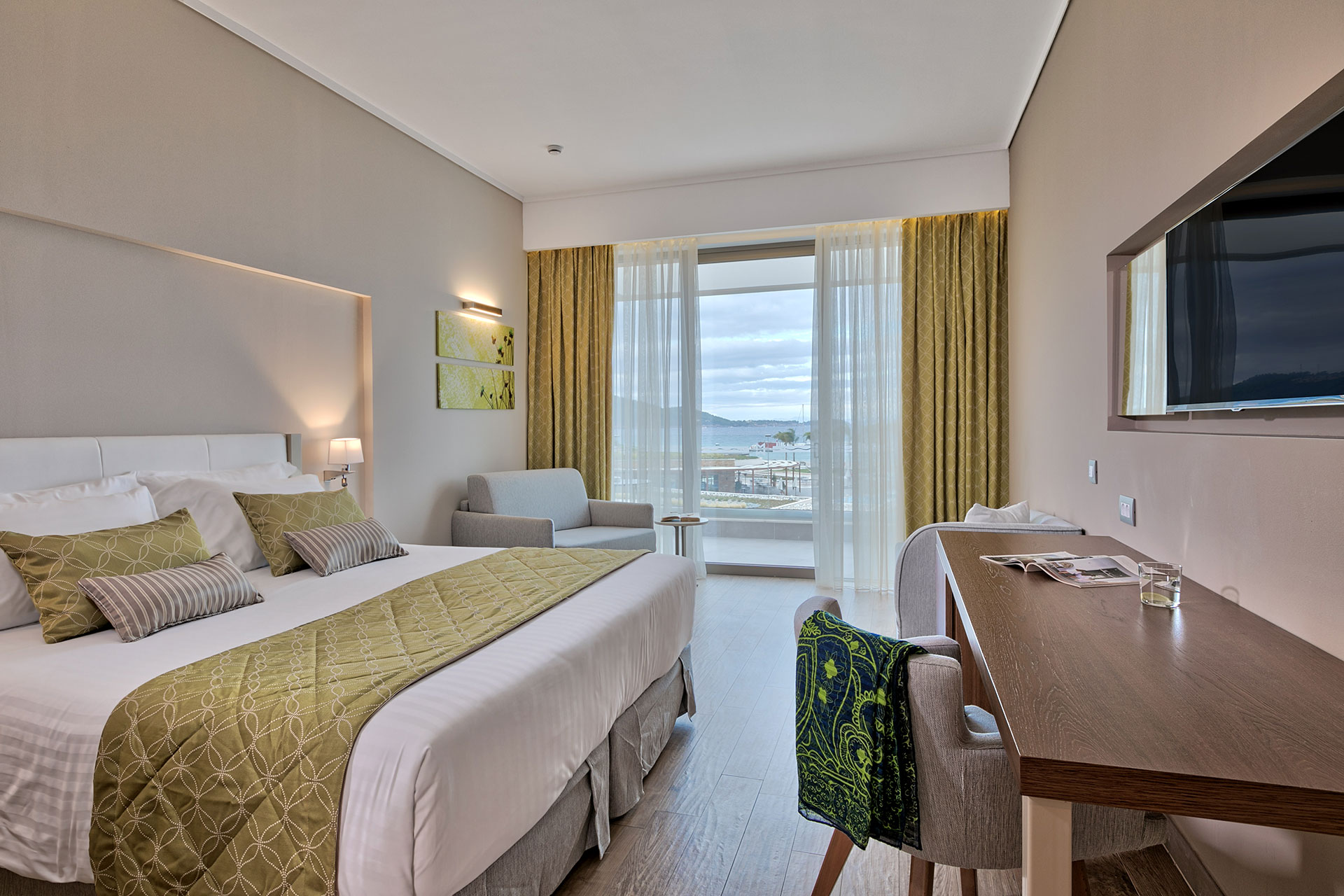 Modern deluxe room with olive-green accents, desk area, and balcony overlooking the Aegean
