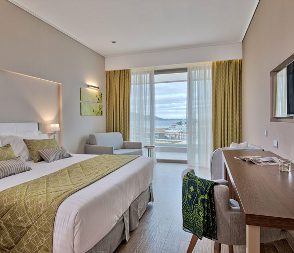 Modern deluxe room with olive-green accents, desk area, and balcony overlooking the Aegean