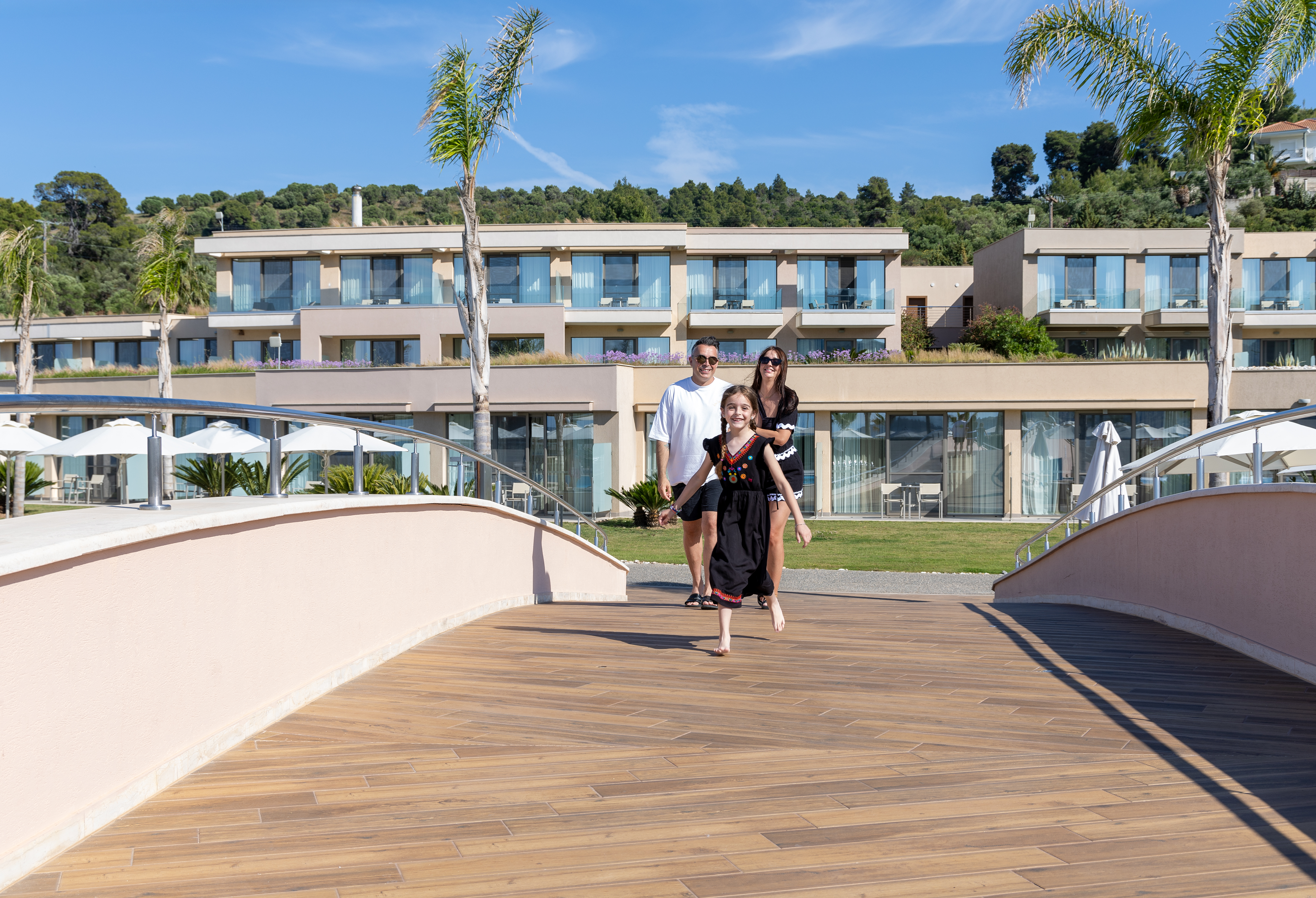 Family enjoying a sunny walk across the resort bridge with modern suites in the background