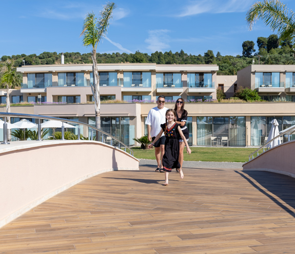Family enjoying a sunny walk across the resort bridge with modern suites in the background
