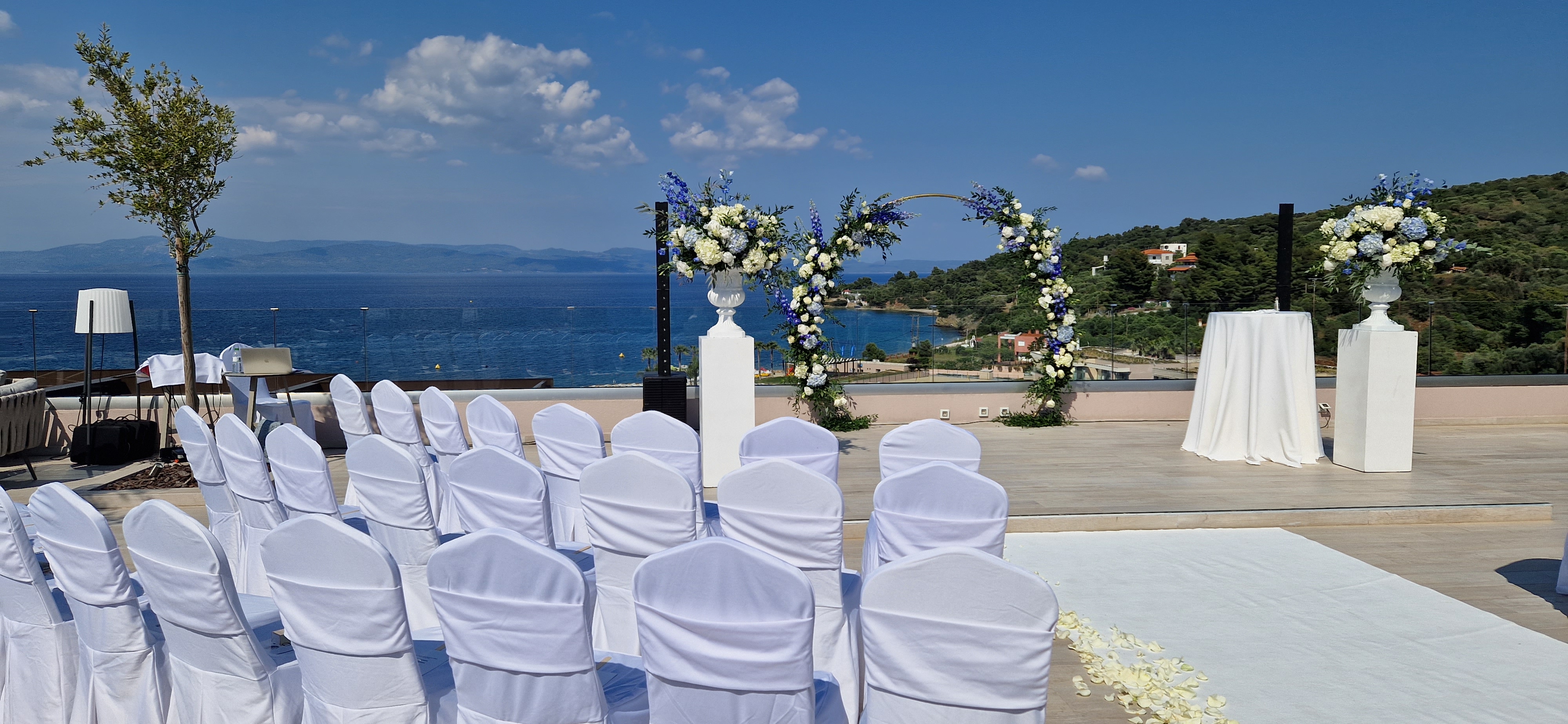 Outdoor wedding ceremony setup with floral arch and white chairs overlooking the sea