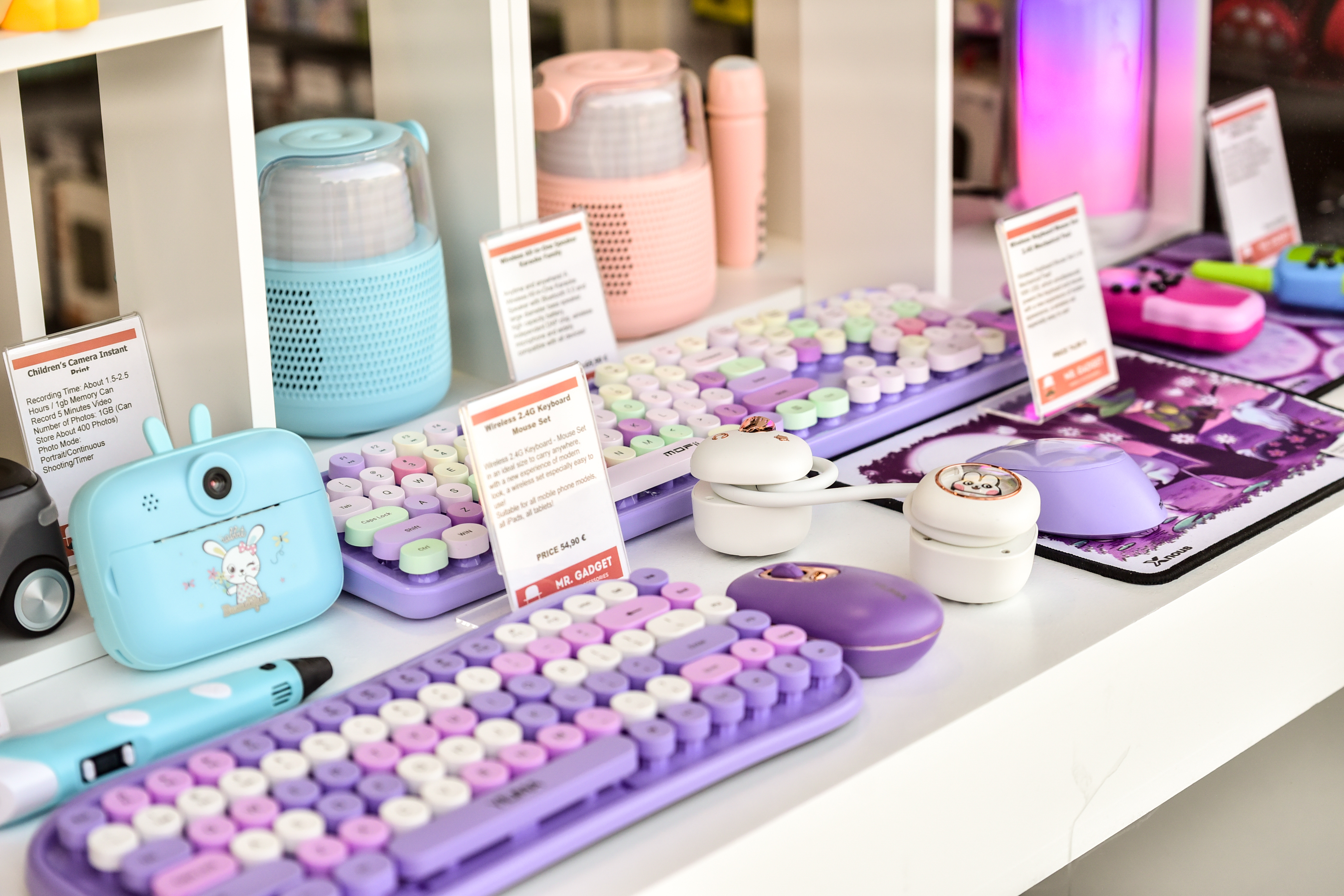 Colorful wireless keyboards, headphones, and cute mini cameras displayed on tech counter