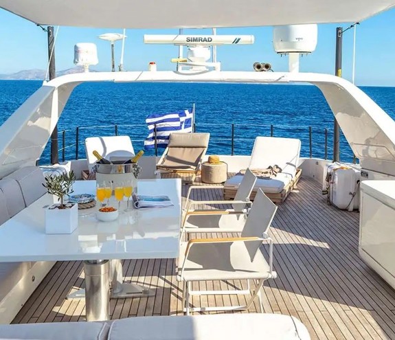 Sunny deck of a luxury yacht with loungers, dining table and drinks set against deep blue sea