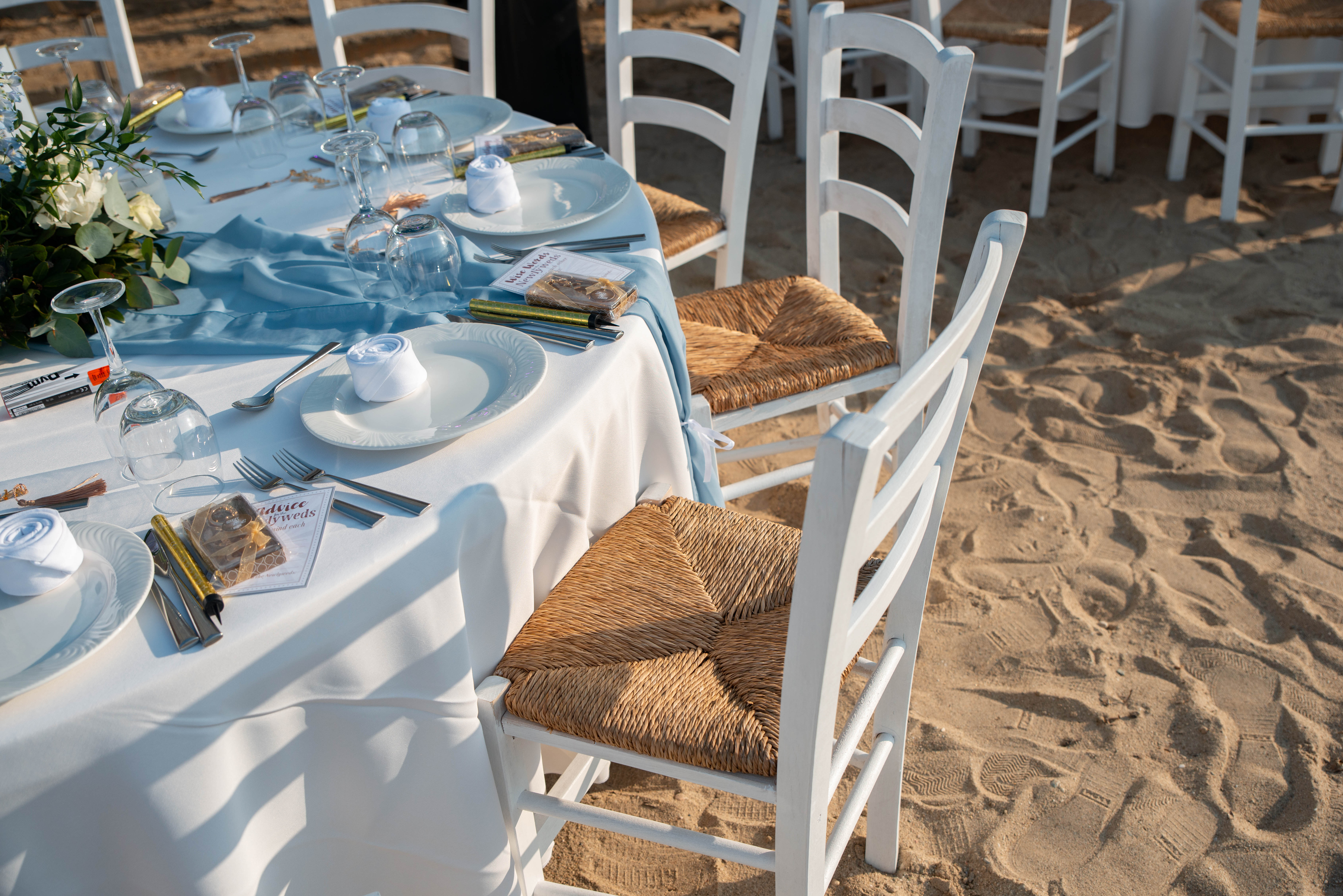 Beach wedding table with white linens, rustic chairs, and light blue decorations 