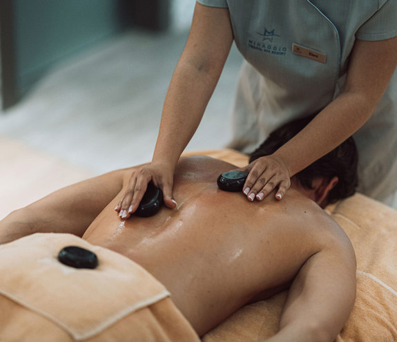 Therapist performing relaxing hot stone massage on guest's back