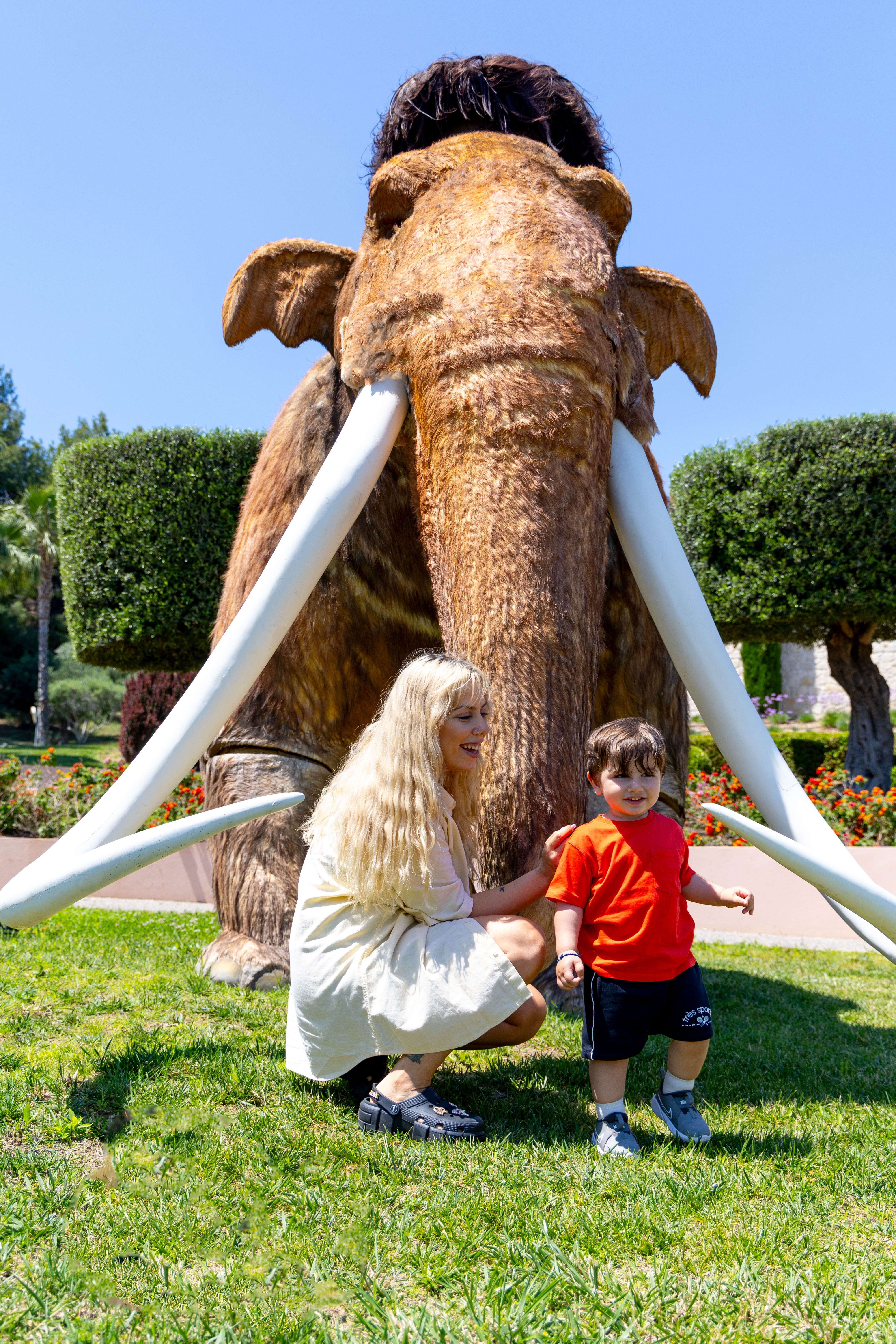 Mother and child smiling in front of a large mammoth statue at Kids Planet