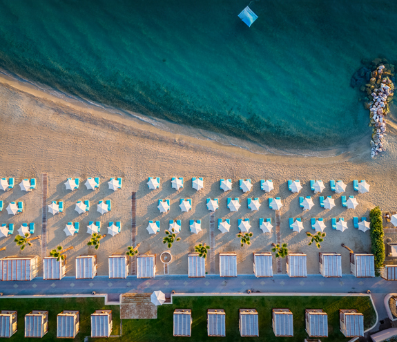 Top down aerial view of the beach with turquoise cabanas, umbrellas, and calm clear sea