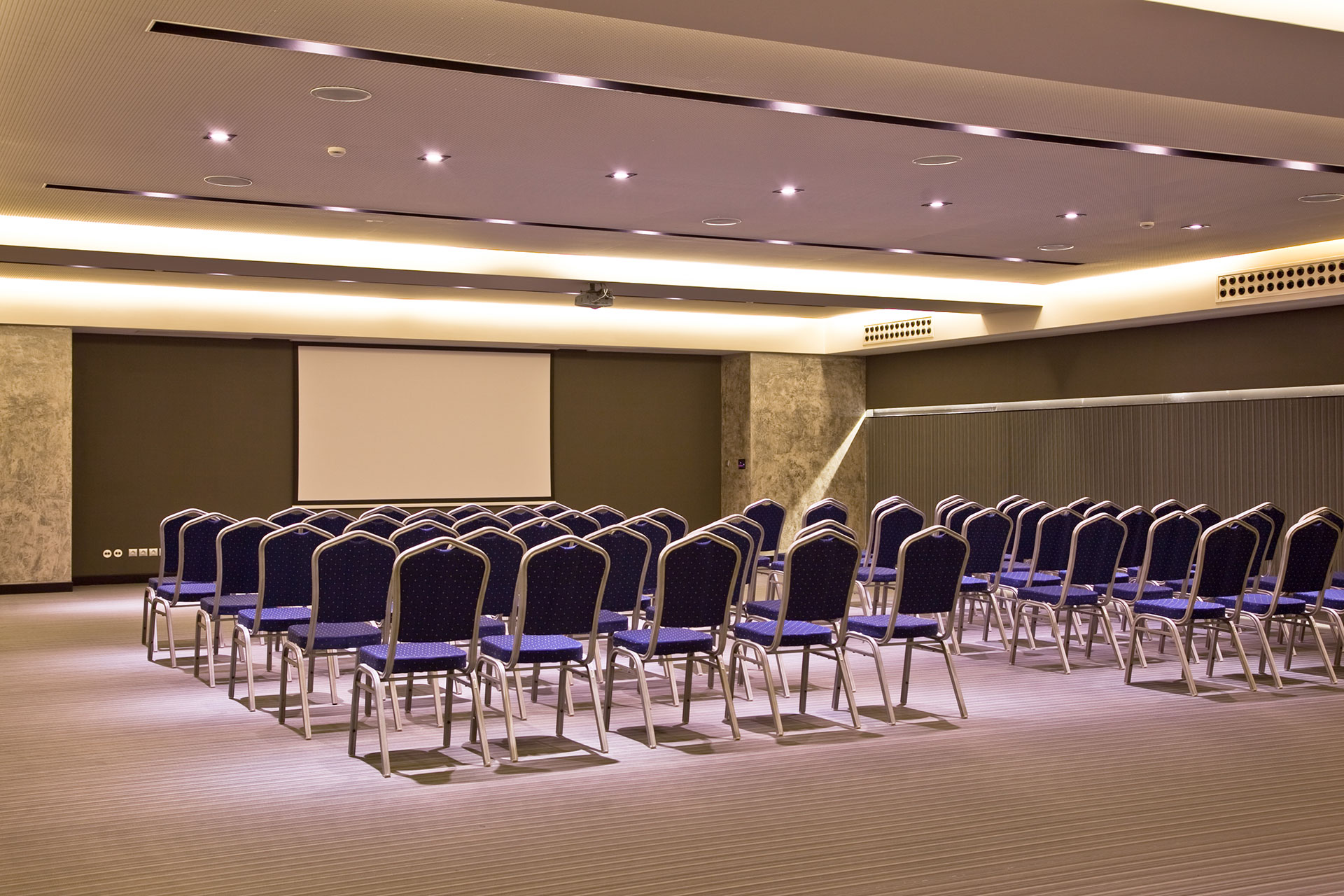 Elegant conference hall with modern lighting and rows of blue chairs facing a projector screen