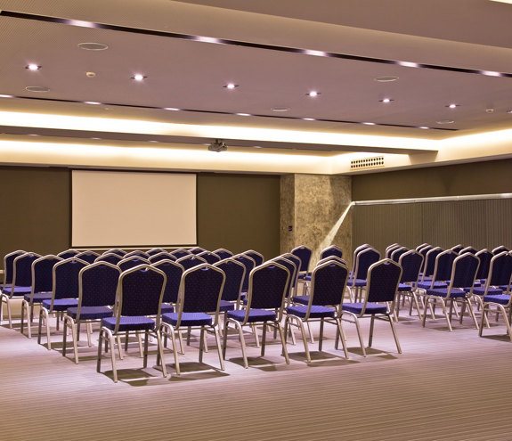 Elegant conference hall with modern lighting and rows of blue chairs facing a projector screen