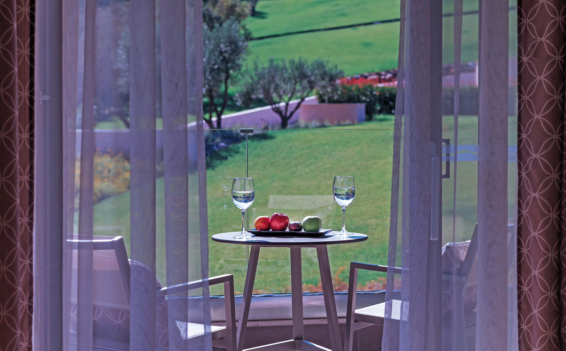 Balcony view from superior room with chairs, apples and wine glasses overlooking lush gardens