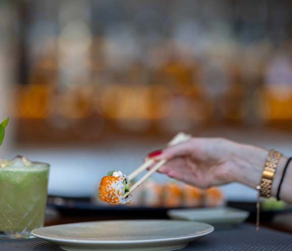 Sushi Bar sushi bite picked up with chopsticks and a mojito on the side