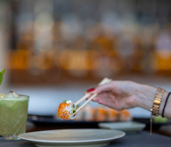 Sushi Bar sushi bite picked up with chopsticks and a mojito on the side