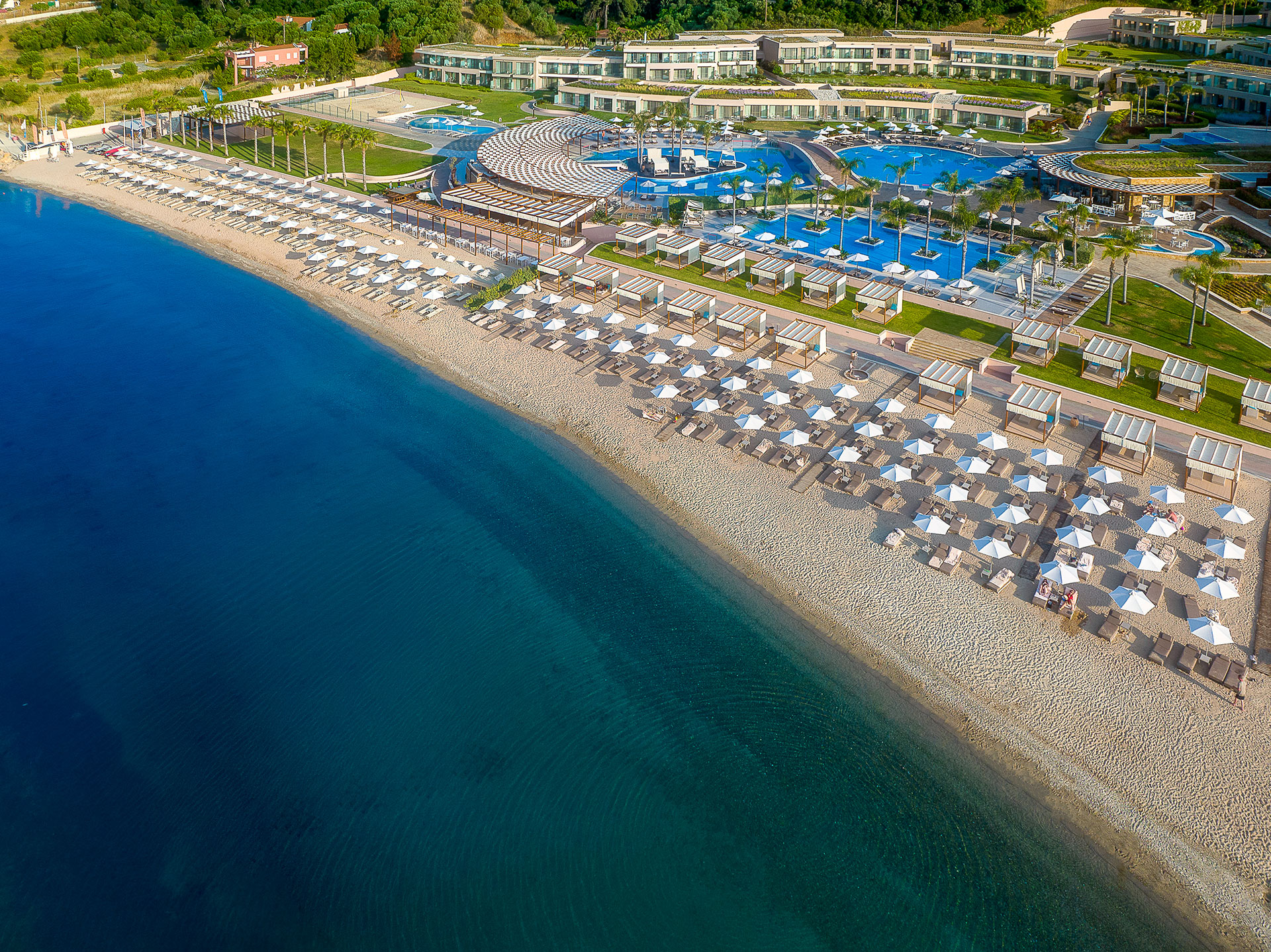 Aerial view of the beachfront with sunbeds, umbrellas, and turquoise sea beside the pools