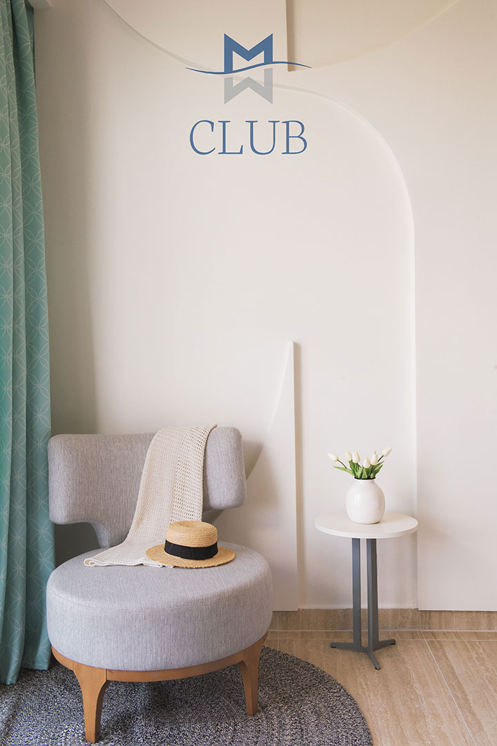Elegant corner of the suite with green curtain, designer chair holding straw hat and towel, and vase on side table