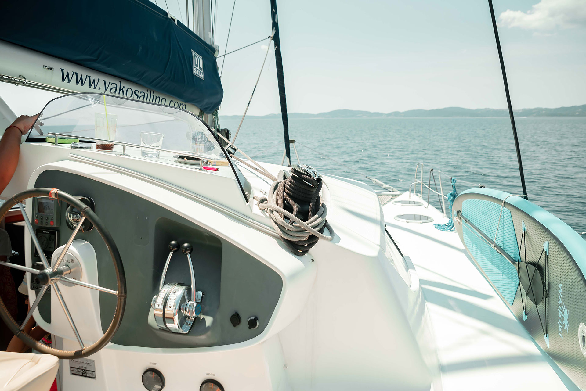 View from the helm of a sailing catamaran cruising on calm blue waters with a paddleboard on deck