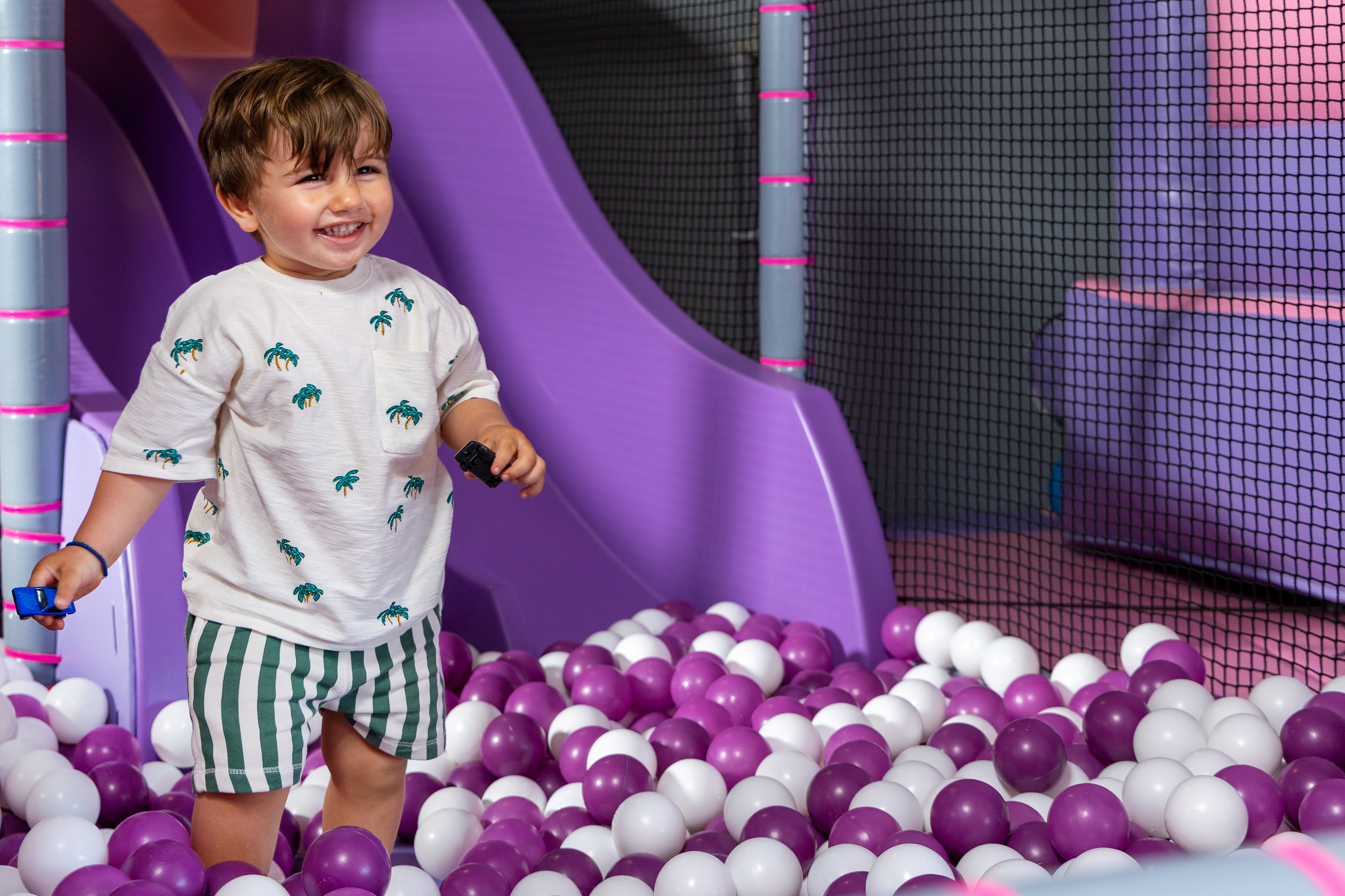 Smiling toddler playing in a purple and white ball pit with slide in Kids Planet