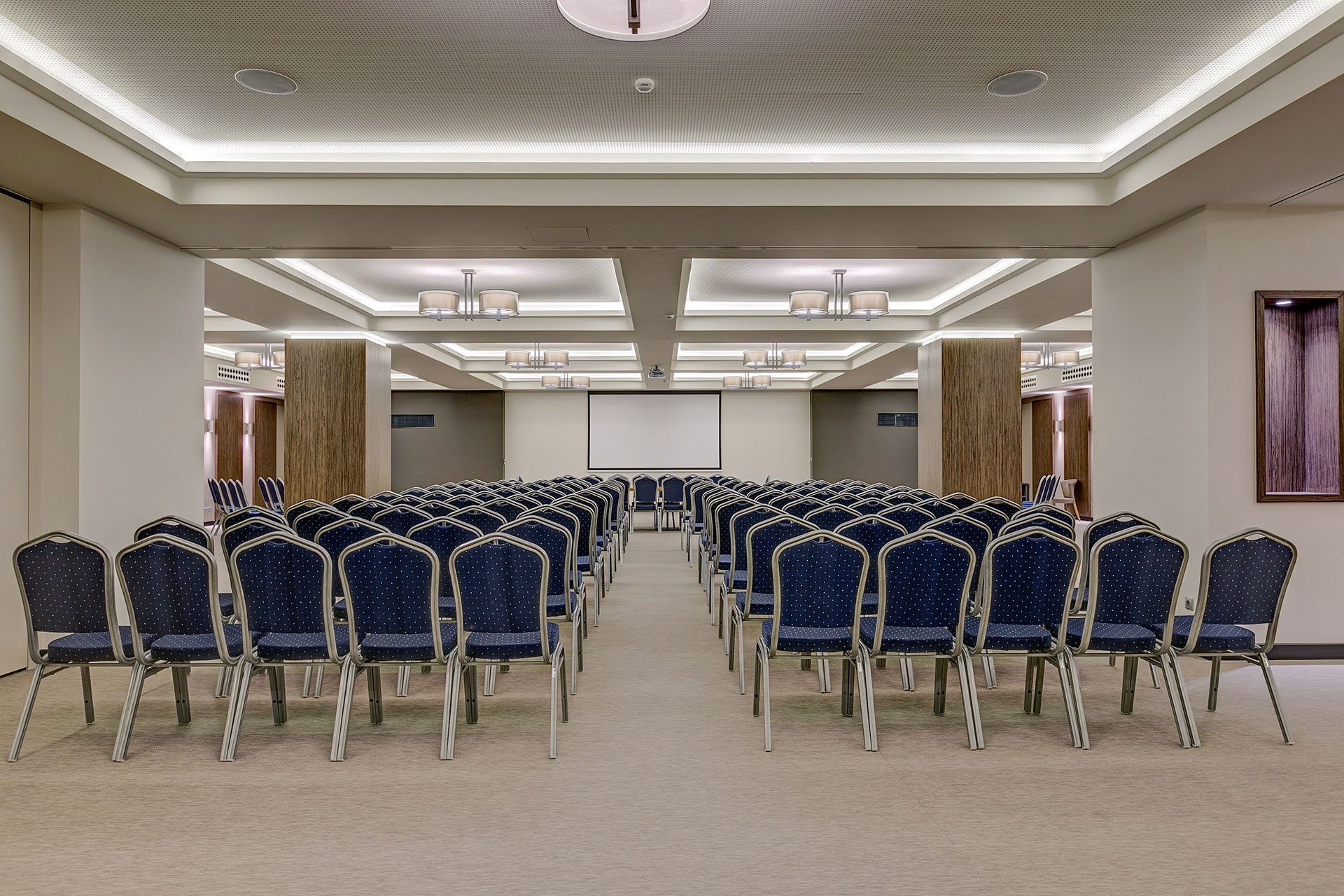 Spacious conference room with rows of blue chairs and projection screen