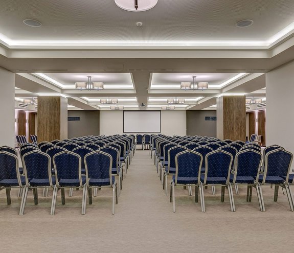 Spacious conference room with rows of blue chairs and projection screen