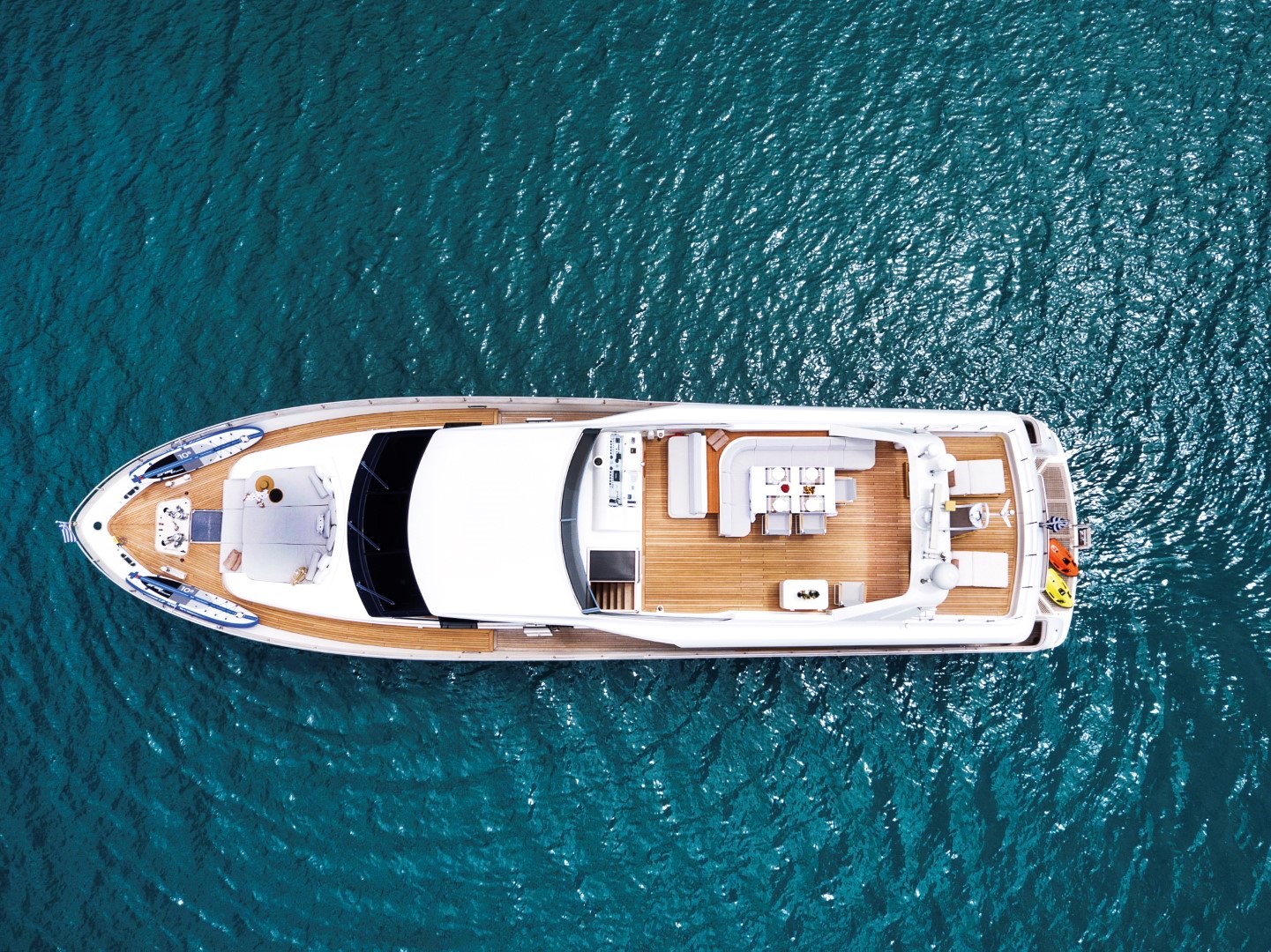 Aerial view of a luxury yacht with spacious sun deck and seating areas floating on clear turquoise water