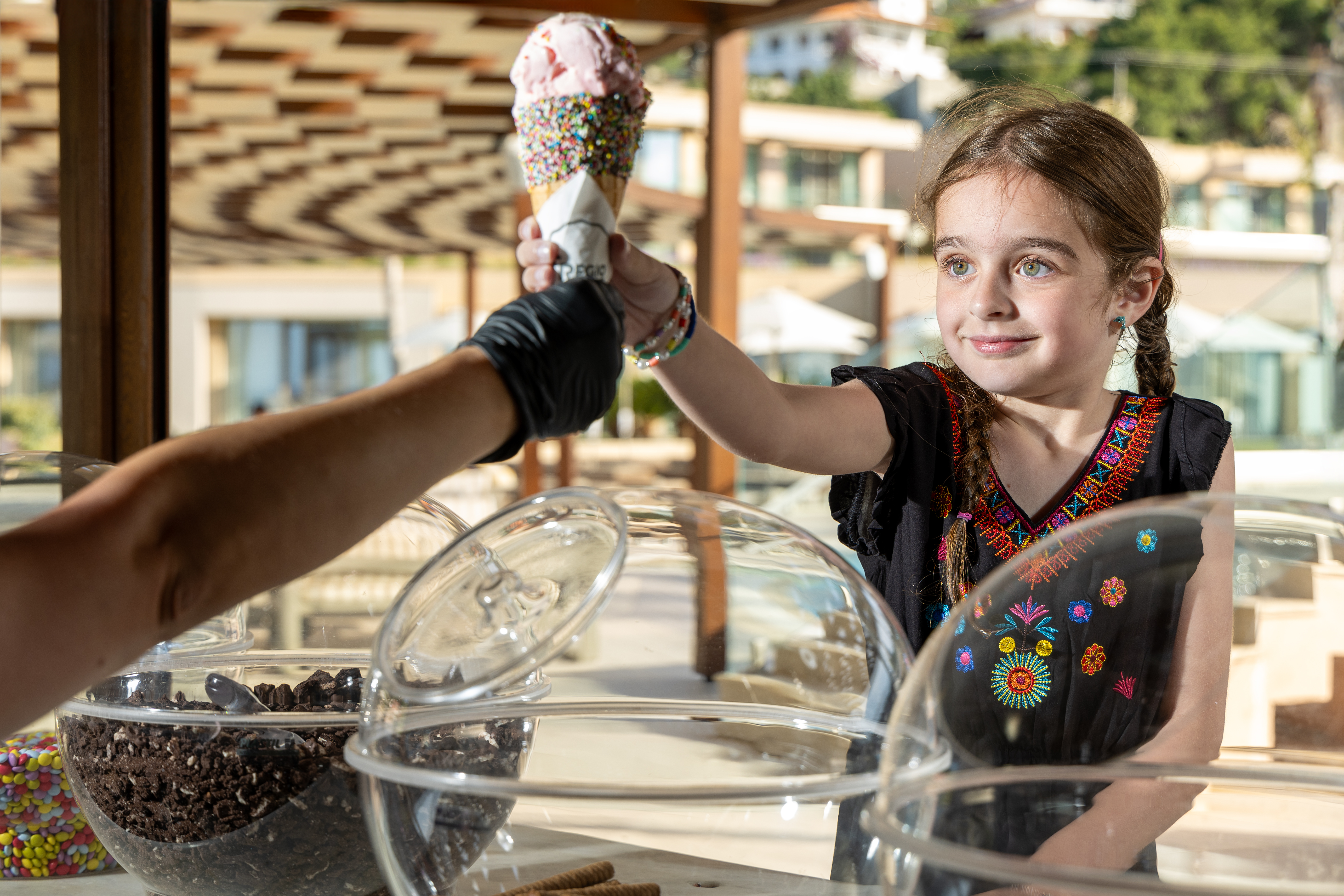 Smiling girl receiving a Fregio ice cream with colorful sprinkles at outdoor counter