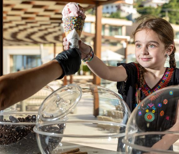 Smiling girl receiving a Fregio ice cream with colorful sprinkles at outdoor counter