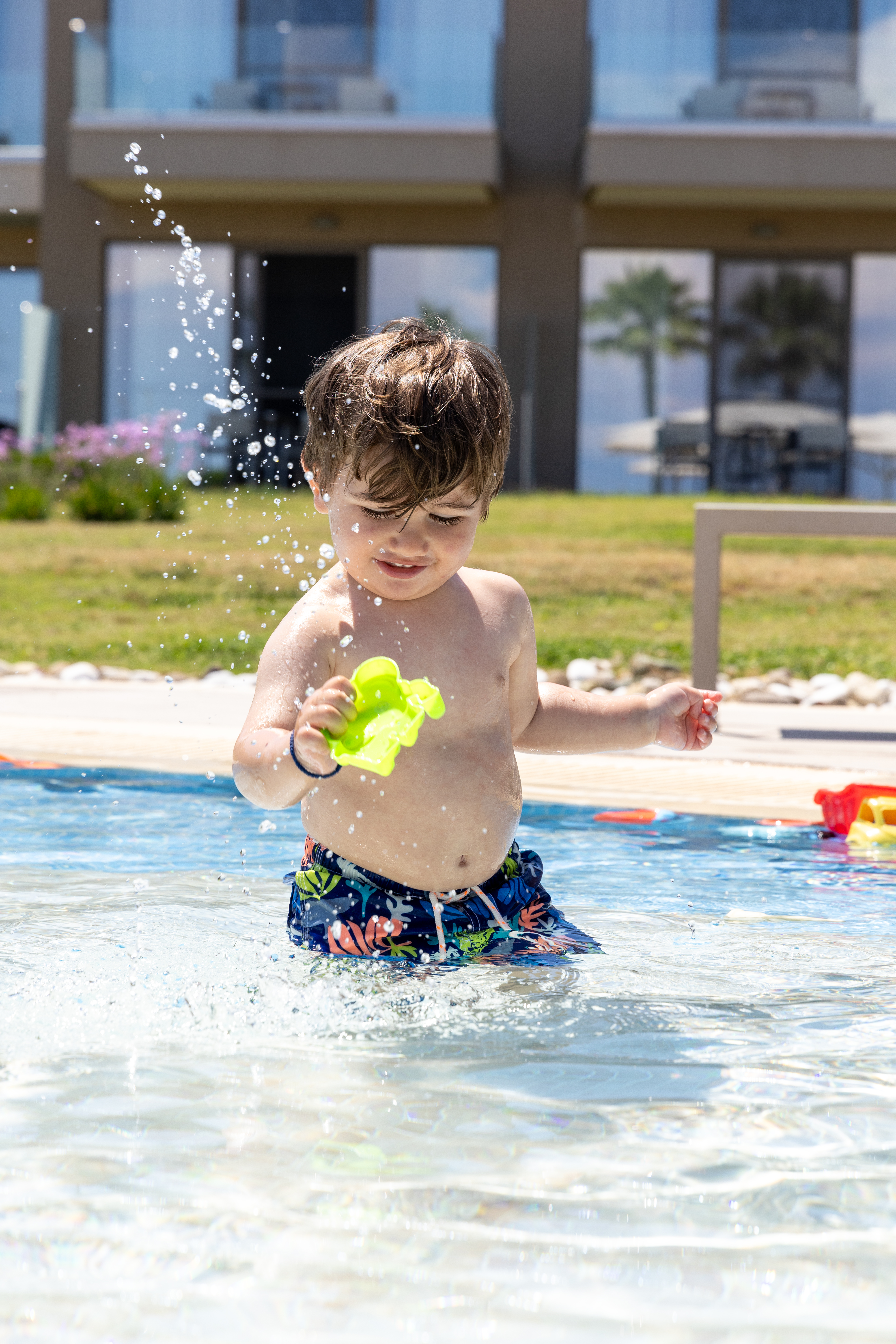 Smiling toddler playing with water toys and splashing in the kids' pool under the sun