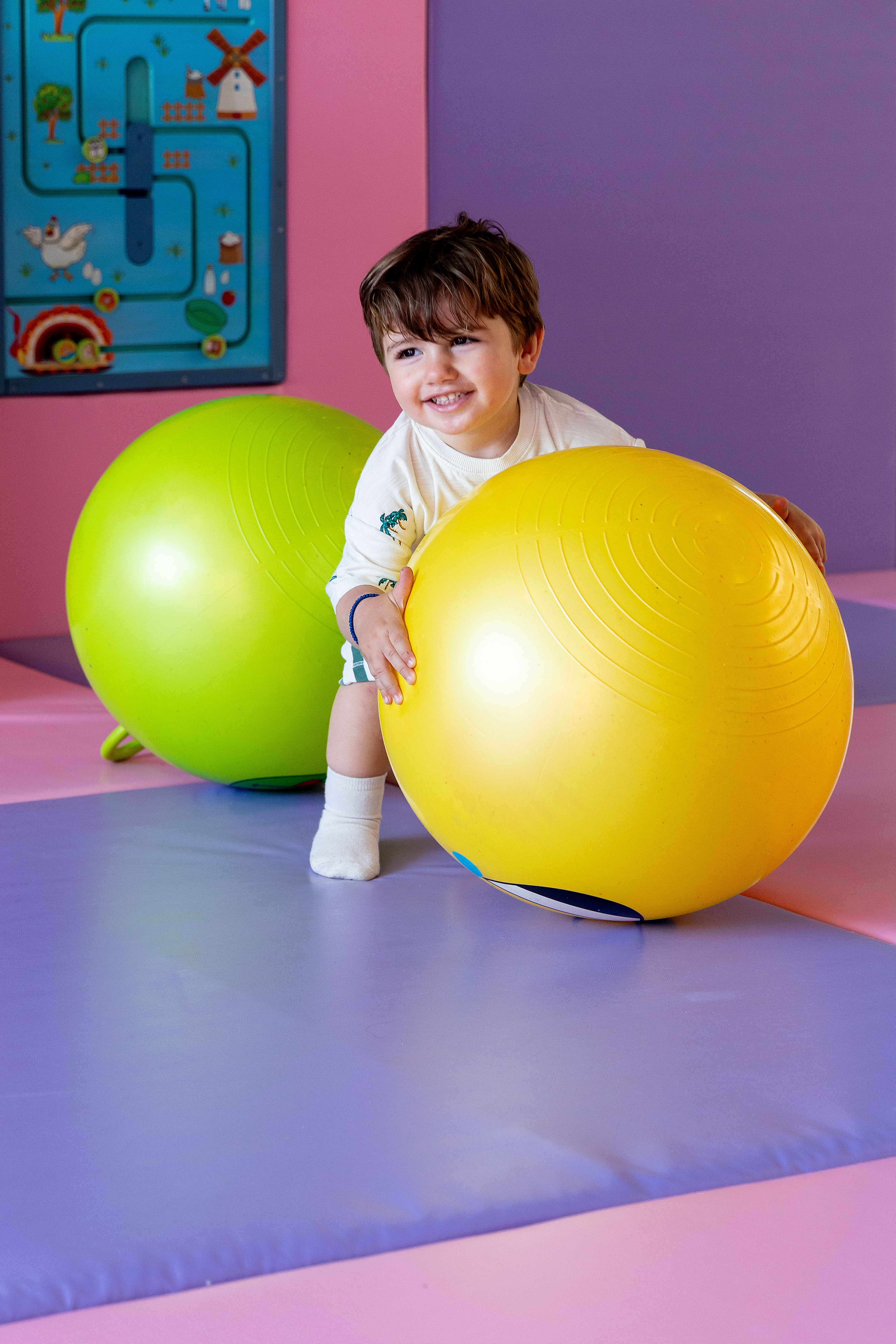 Happy toddler playing with bright yellow and green balls at the indoor Kids Planet 