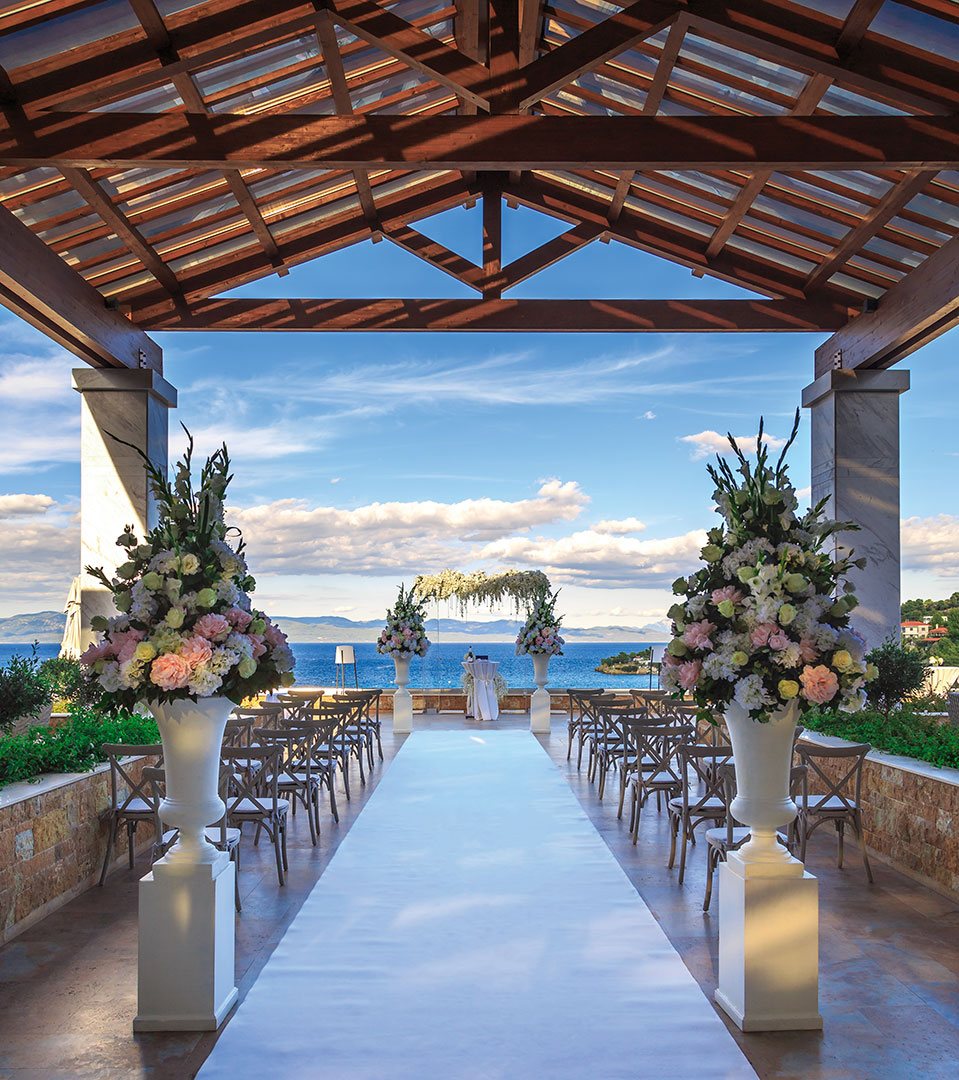 Elegant wedding ceremony setup under wooden pergola with sea view and floral arch