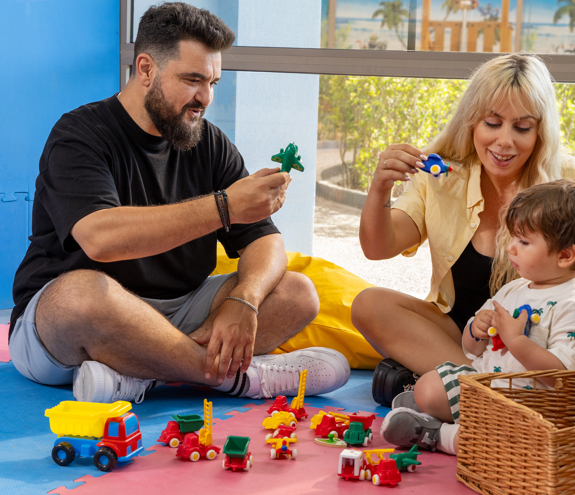 Parents playing with their toddler on colorful mats with toy cars and airplanes