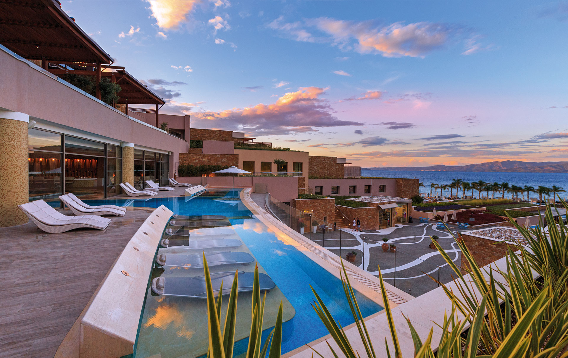 Thermal spa pool with hydro loungers overlooking the sea at sunset