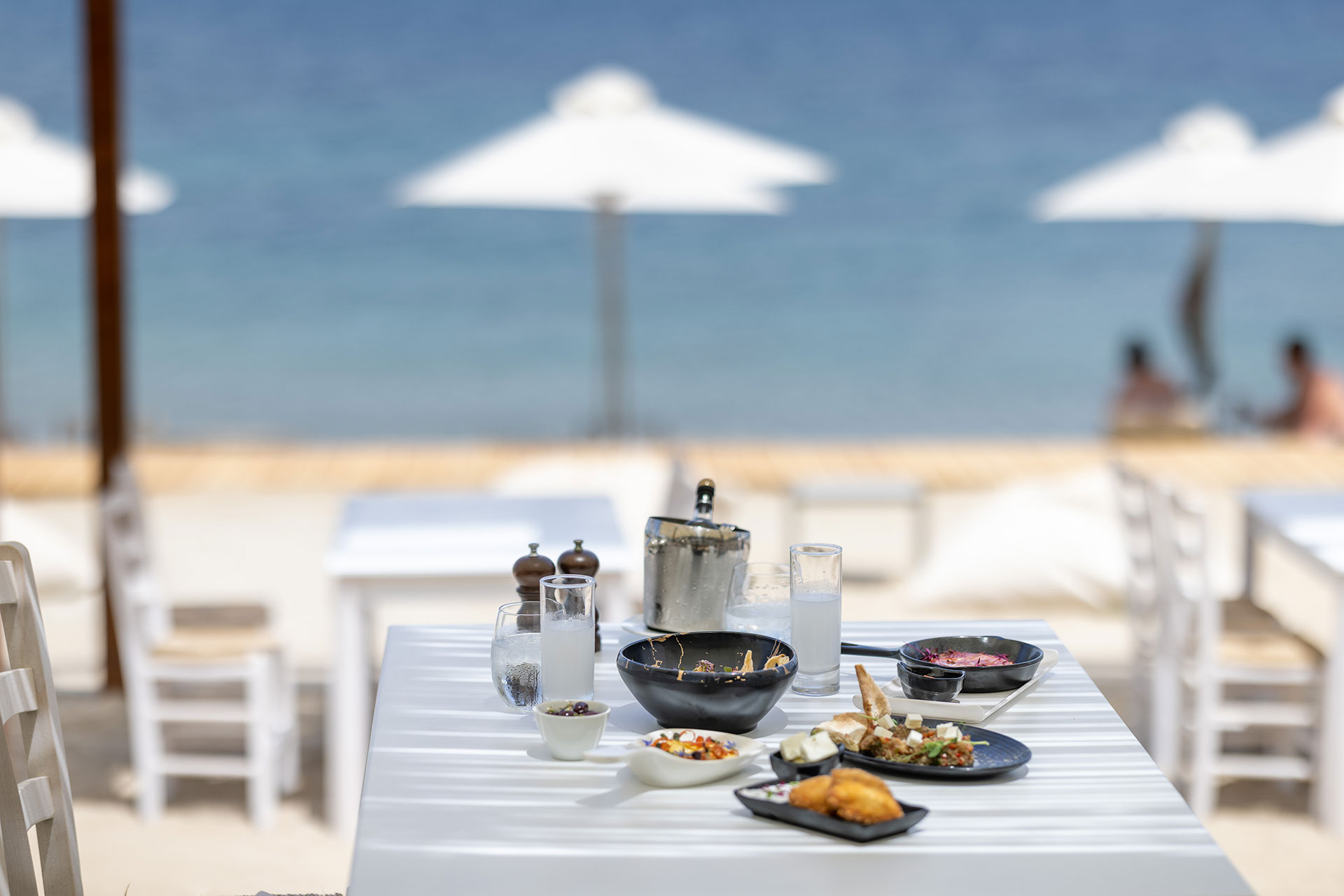 Served table with greek traditional small plates, glasses of ouzo and sea view in Mezedaki beach restaurant
