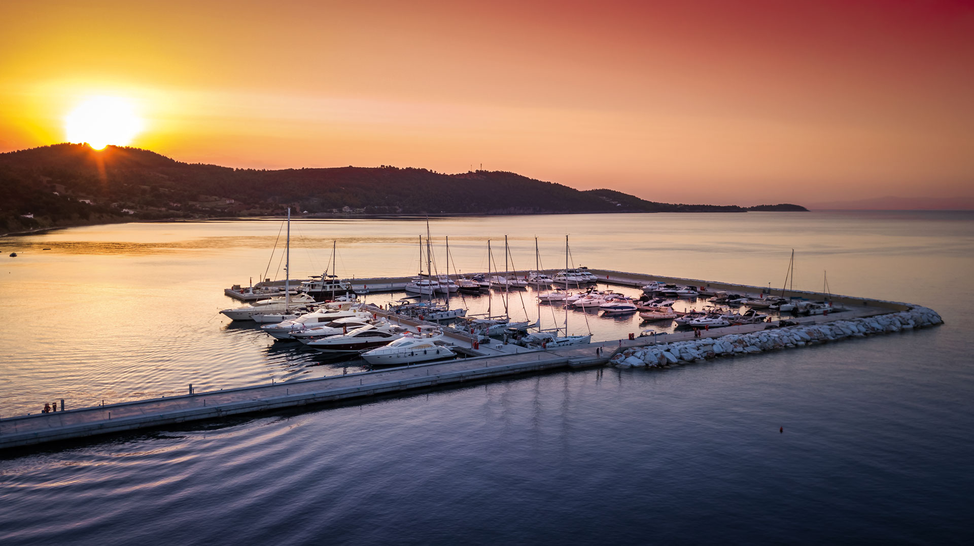 Aerial view of luxury yachts docked at the marina under a golden sunset sky