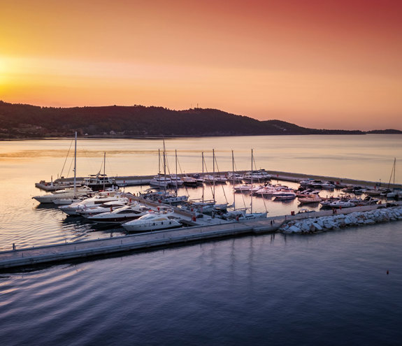 Aerial view of luxury yachts docked at the marina under a golden sunset sky