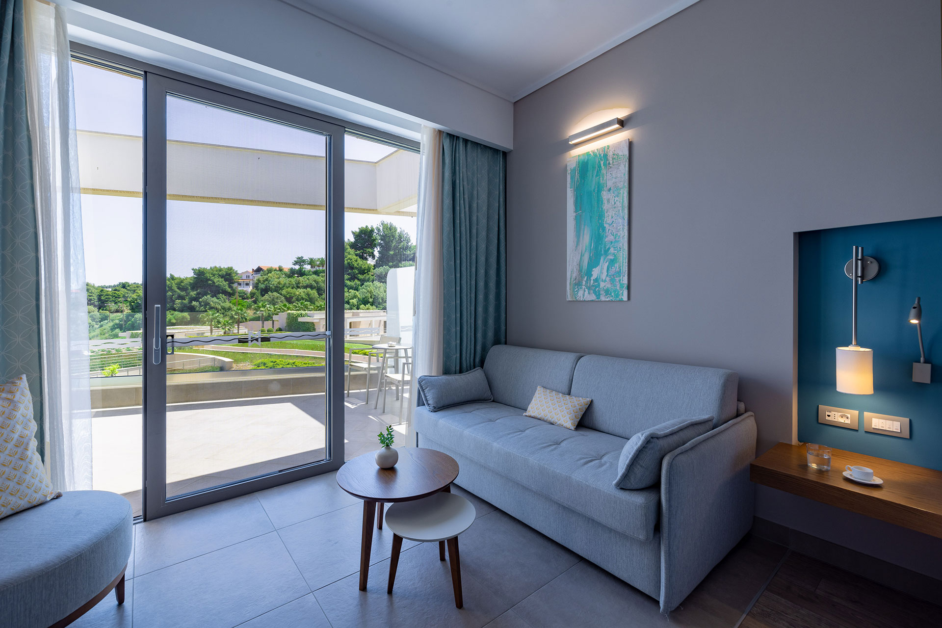 Cozy sitting area with sofa and terrace access overlooking lush gardens and the sea