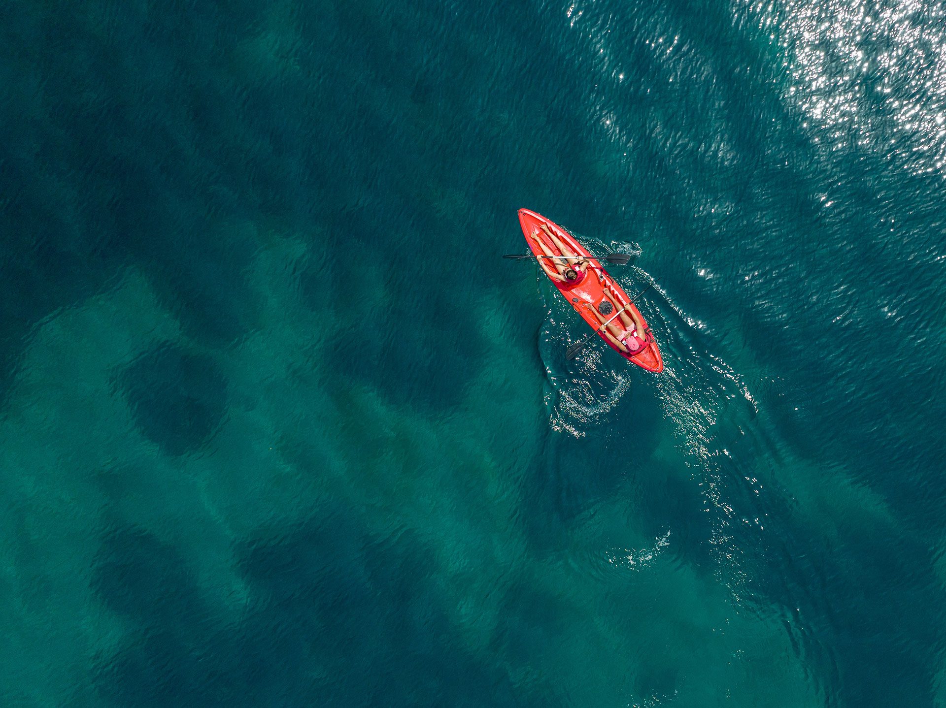Couple kayaking in a bright red kayak over clear turquoise sea waters