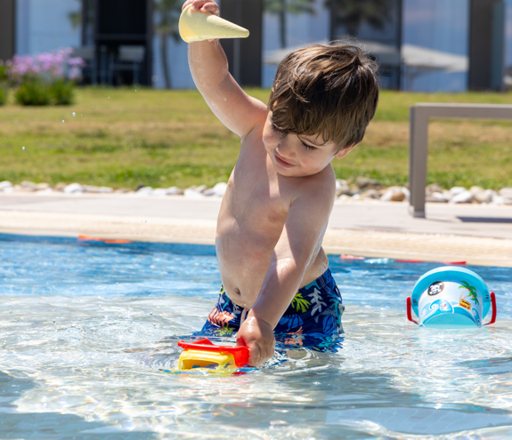 Young boy playing with colorful toys in the kids' pool under the sun
