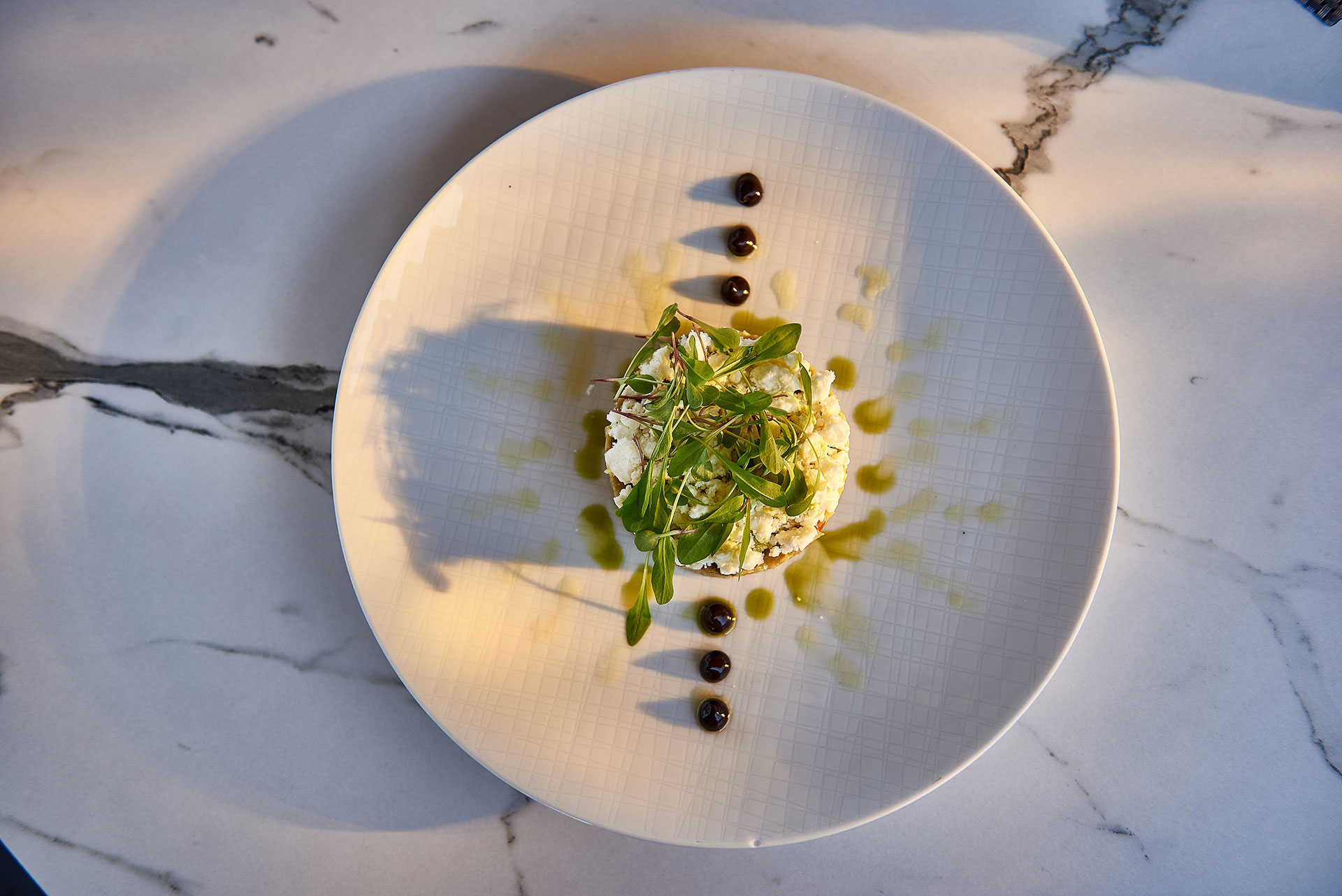 Tartare topped with microgreens and olive oil drizzle, elegantly plated on marble table
