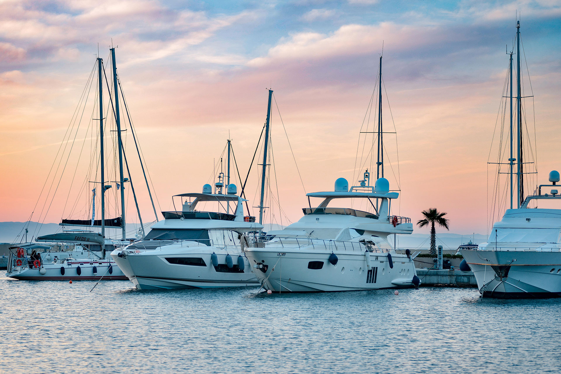 Luxury yachts docked at the marina under a colorful sunset sky with calm waters