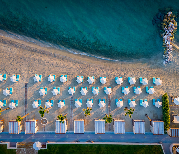 Top down view of the organized sandy beach with sunbeds, umbrellas, and a small rocky pier extending in the sea