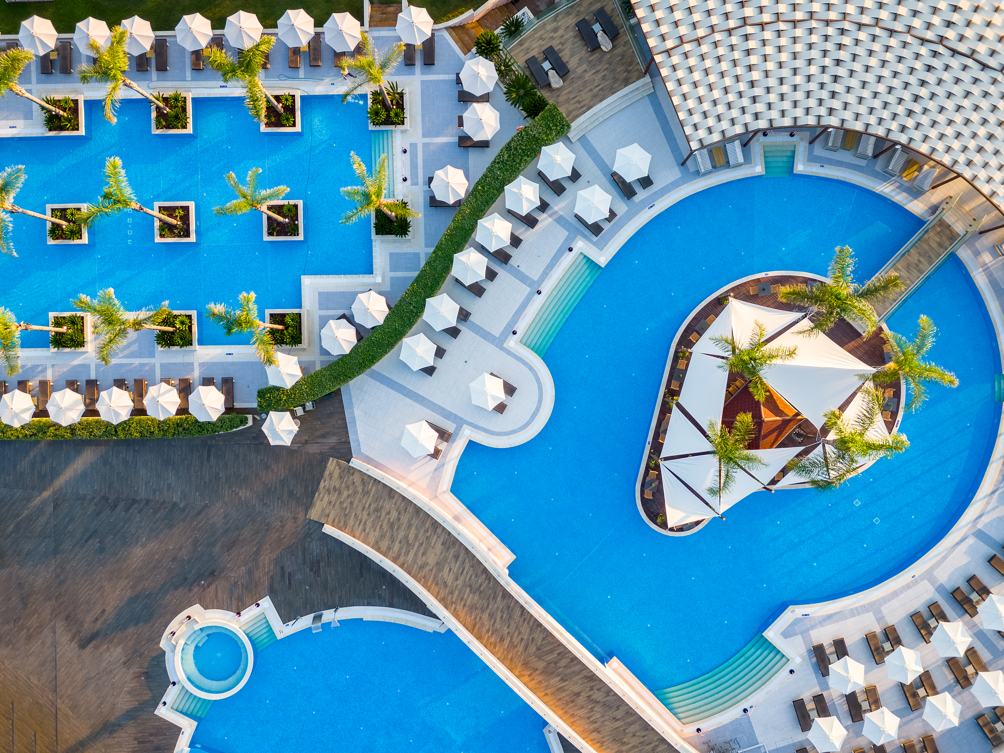 Aerial view of Miraggio Resort pools with geometric design, palm islands and shaded lounge areas