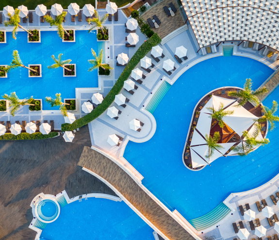 Aerial view of Miraggio Resort pools with geometric design, palm islands and shaded lounge areas