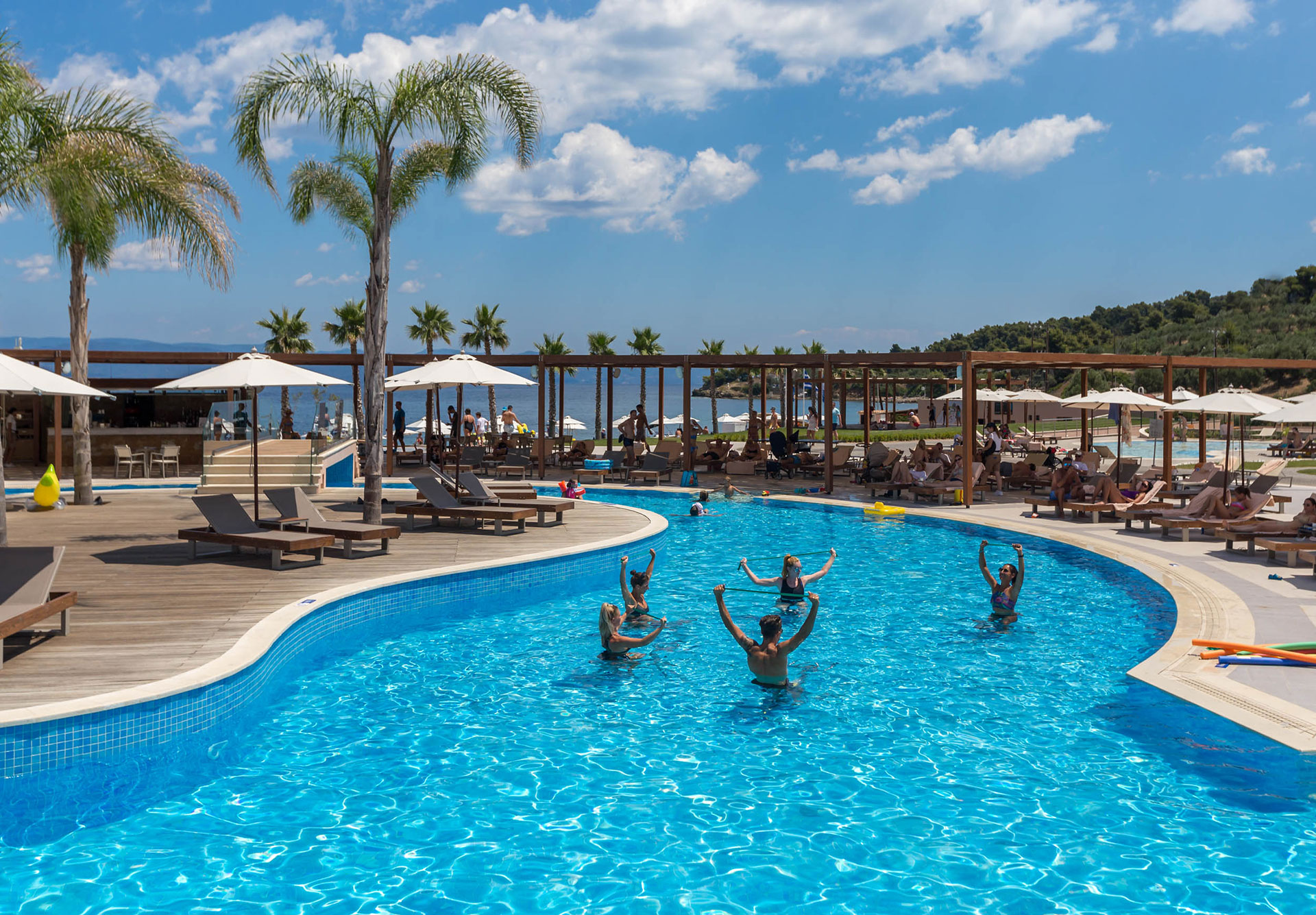 Guests enjoying aqua aerobics in the outdoor pool surrounded by palm trees and sunbeds