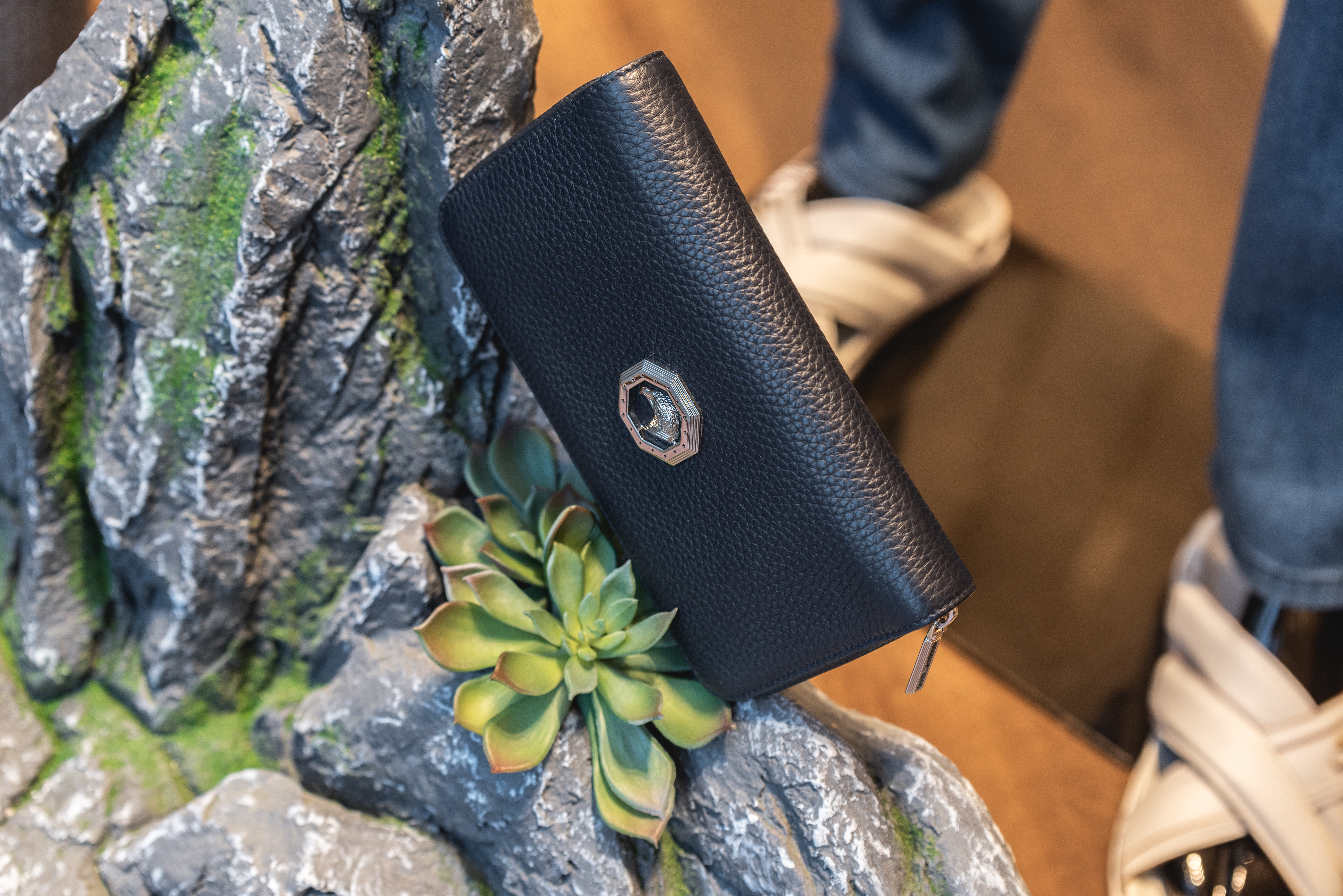 Luxury black leather wallet displayed on rock decor with green succulent detail